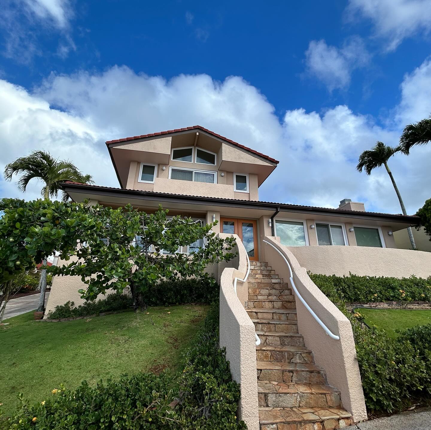 Two-story Oahu home repainted in blush stucco with stone entry stairs and palms